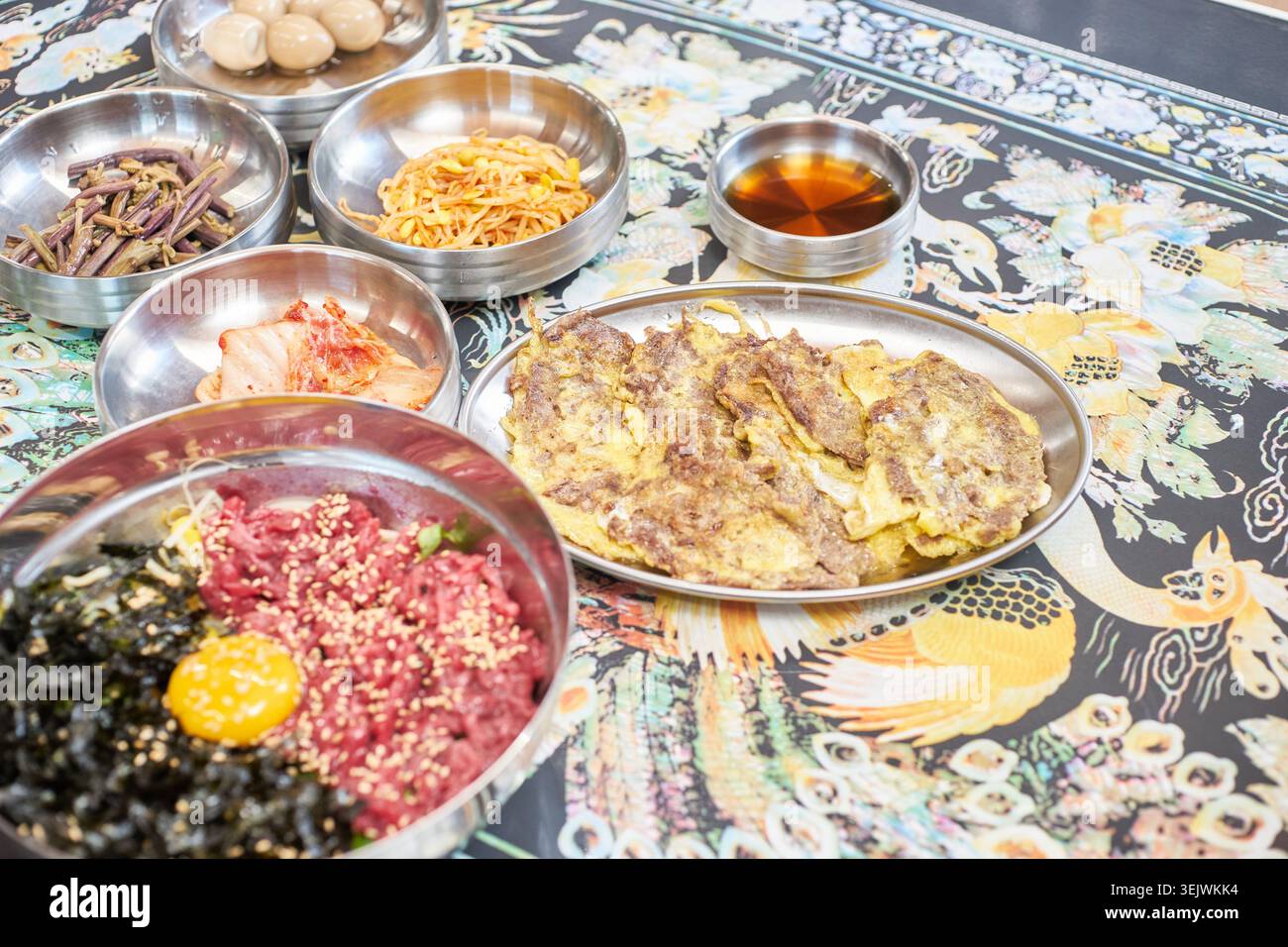 Genießen Sie eine luxuriöse koreanische Mahlzeit mit frischem rohem Rindfleisch-Bibimbap und herzhaftem, in der Pfanne gebratenem Rindfleisch. Diese Kombination bietet eine perfekte kulinarische Harmonie. Stockfoto