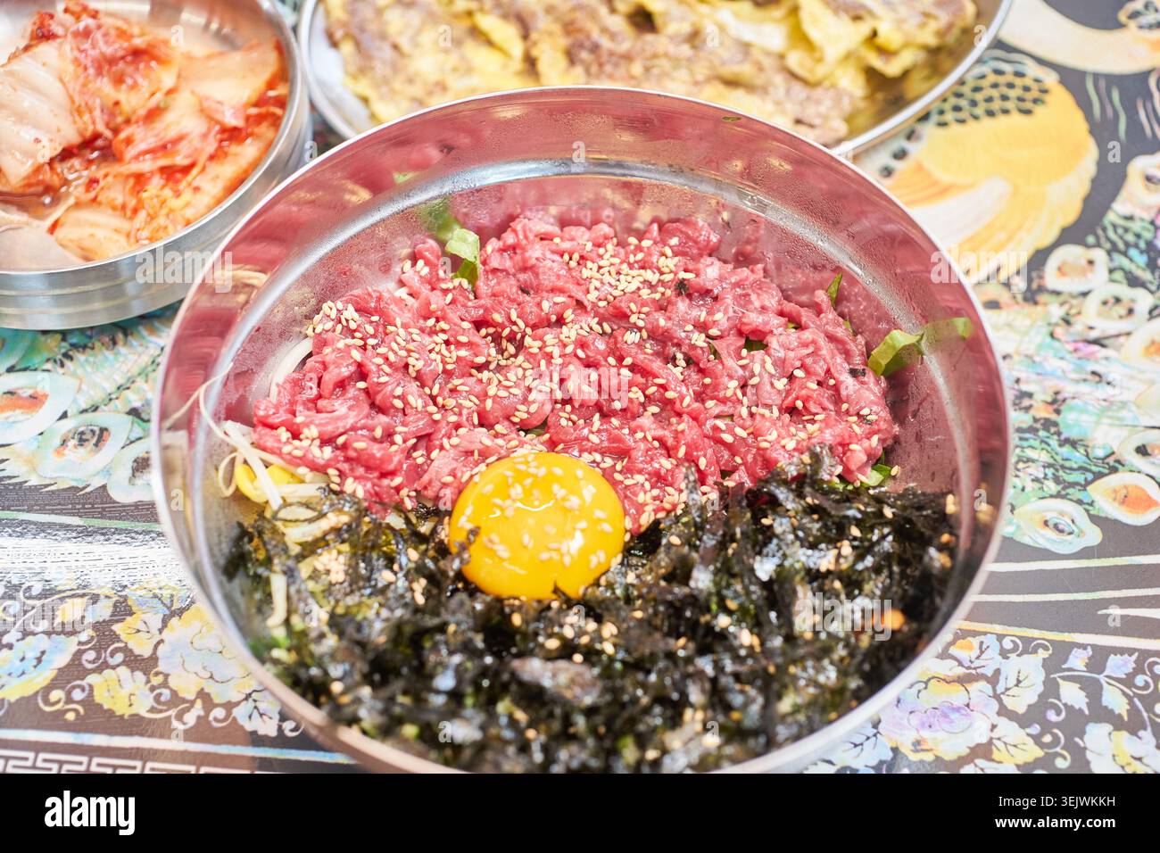 Genießen Sie eine luxuriöse koreanische Mahlzeit mit frischem rohem Rindfleisch-Bibimbap und herzhaftem, in der Pfanne gebratenem Rindfleisch. Diese Kombination bietet eine perfekte kulinarische Harmonie. Stockfoto