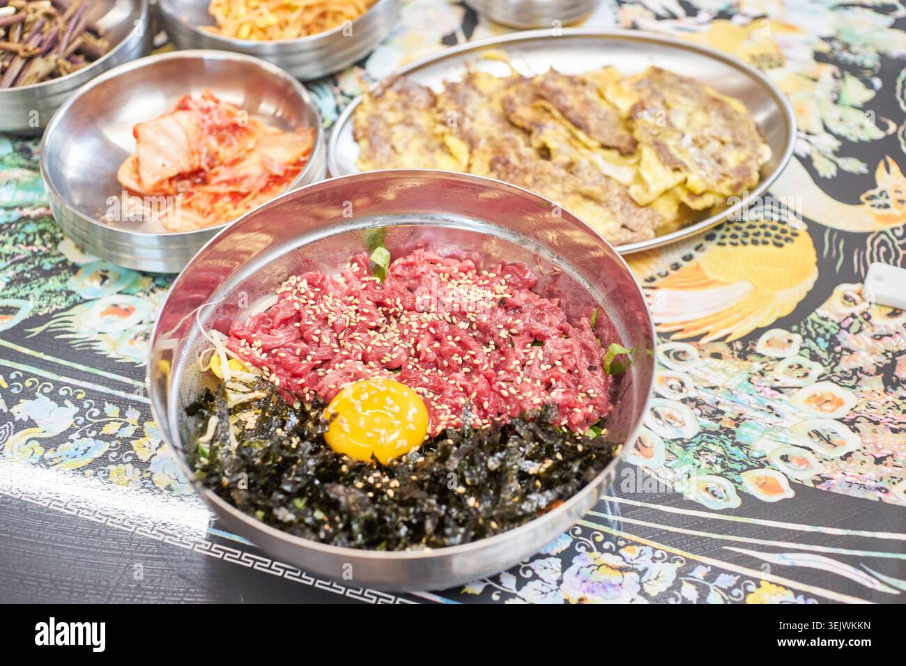 Genießen Sie eine luxuriöse koreanische Mahlzeit mit frischem rohem Rindfleisch-Bibimbap und herzhaftem, in der Pfanne gebratenem Rindfleisch. Diese Kombination bietet eine perfekte kulinarische Harmonie. Stockfoto