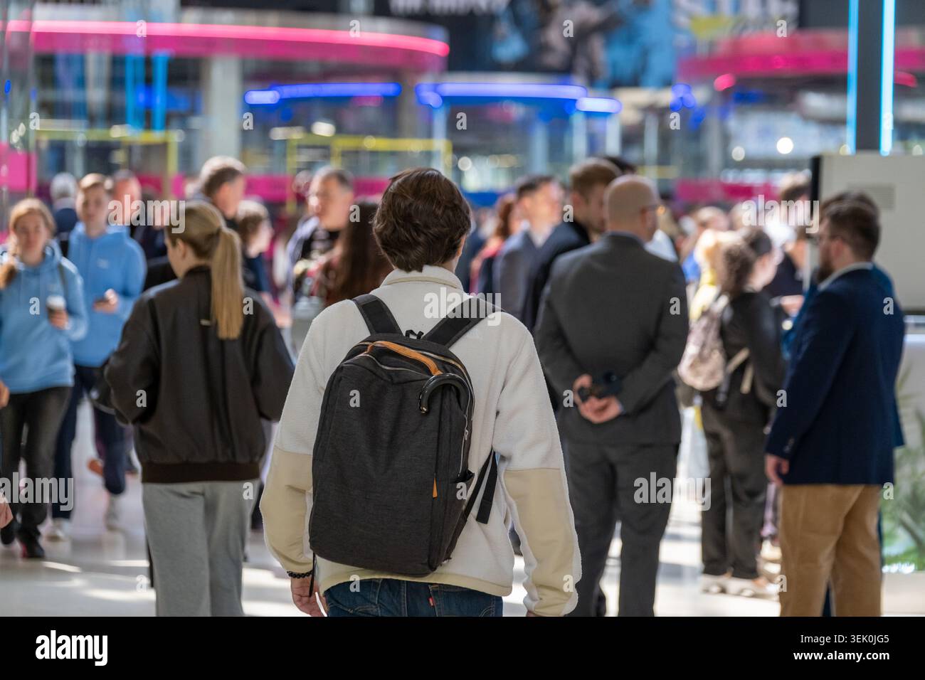 Junge Person mit Rucksack spaziert durch die geschäftige Menge von Pendlern und Einkäufern, die Atmosphäre eines städtischen Einkaufszentrums, Bewegung und Anonymität. Stockfoto