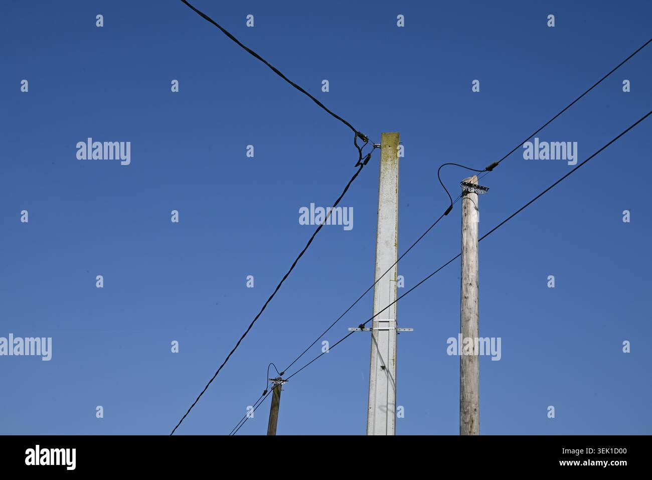 Elektrische Drähte und Pfosten bilden geometrische Formen vor blauem Himmel Stockfoto
