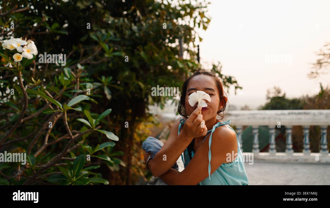 Frau, die in einem Tempelgarten in thailand spielerisch Plumerieblume hält Stockfoto