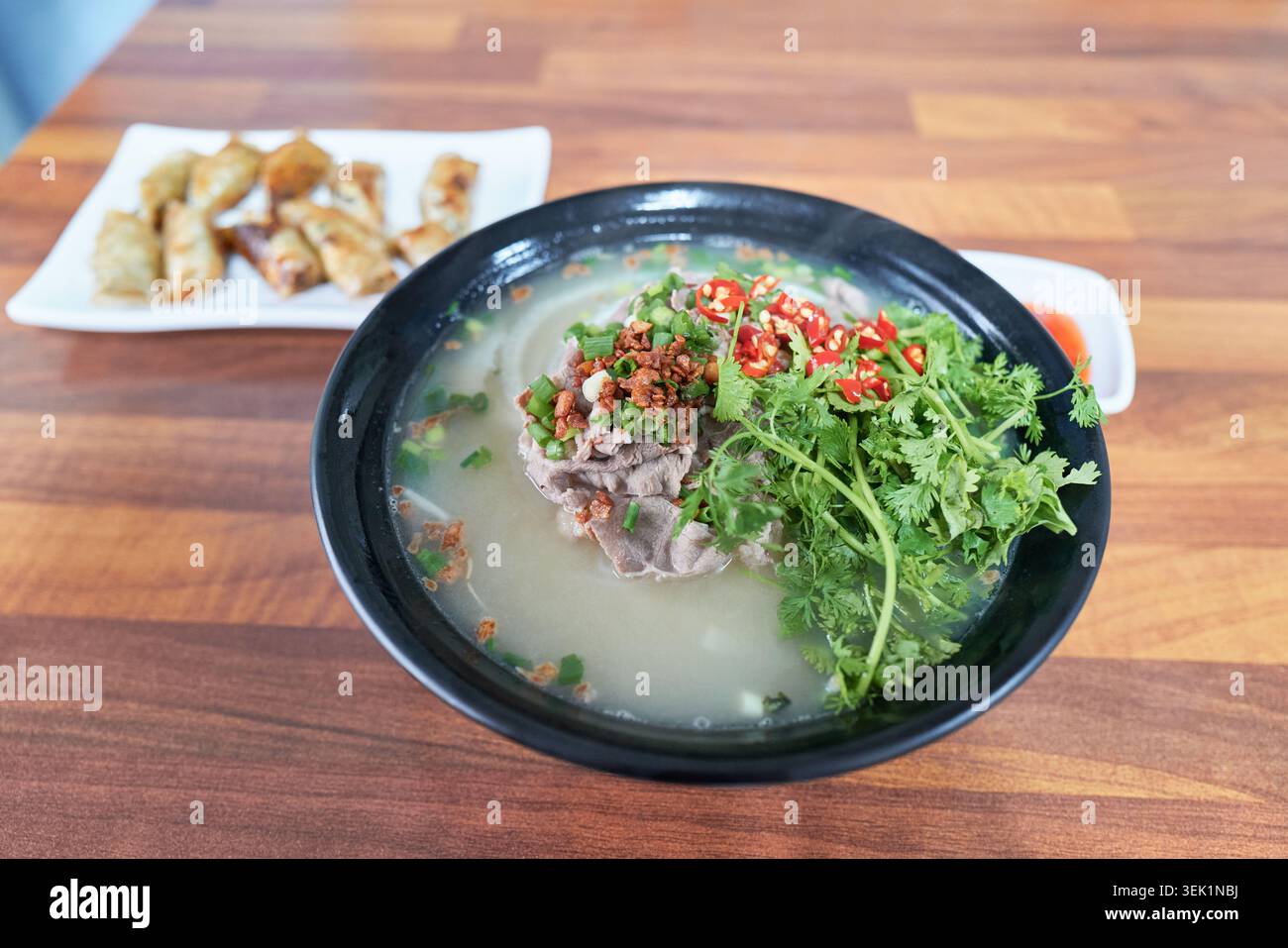 Vietnamesisches Rindfleisch Pho in einer schwarzen Schüssel mit frischem Koriander, Rindfleisch und roten Chilis auf einem Holztisch. Ein perfekter Schuss authentischer asiatischer Speisen. Stockfoto