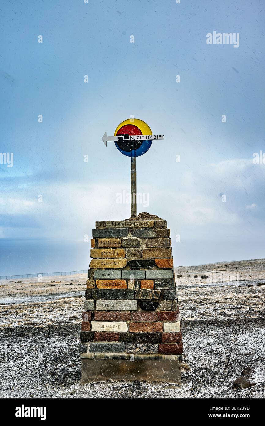 Ein Denkmal am Nordkap in Norwegen mit einem Schild, das die geografische Lage des Nordkap an einem verschneiten Frühlingstag im April markiert. Vertikal mit Kopie Stockfoto