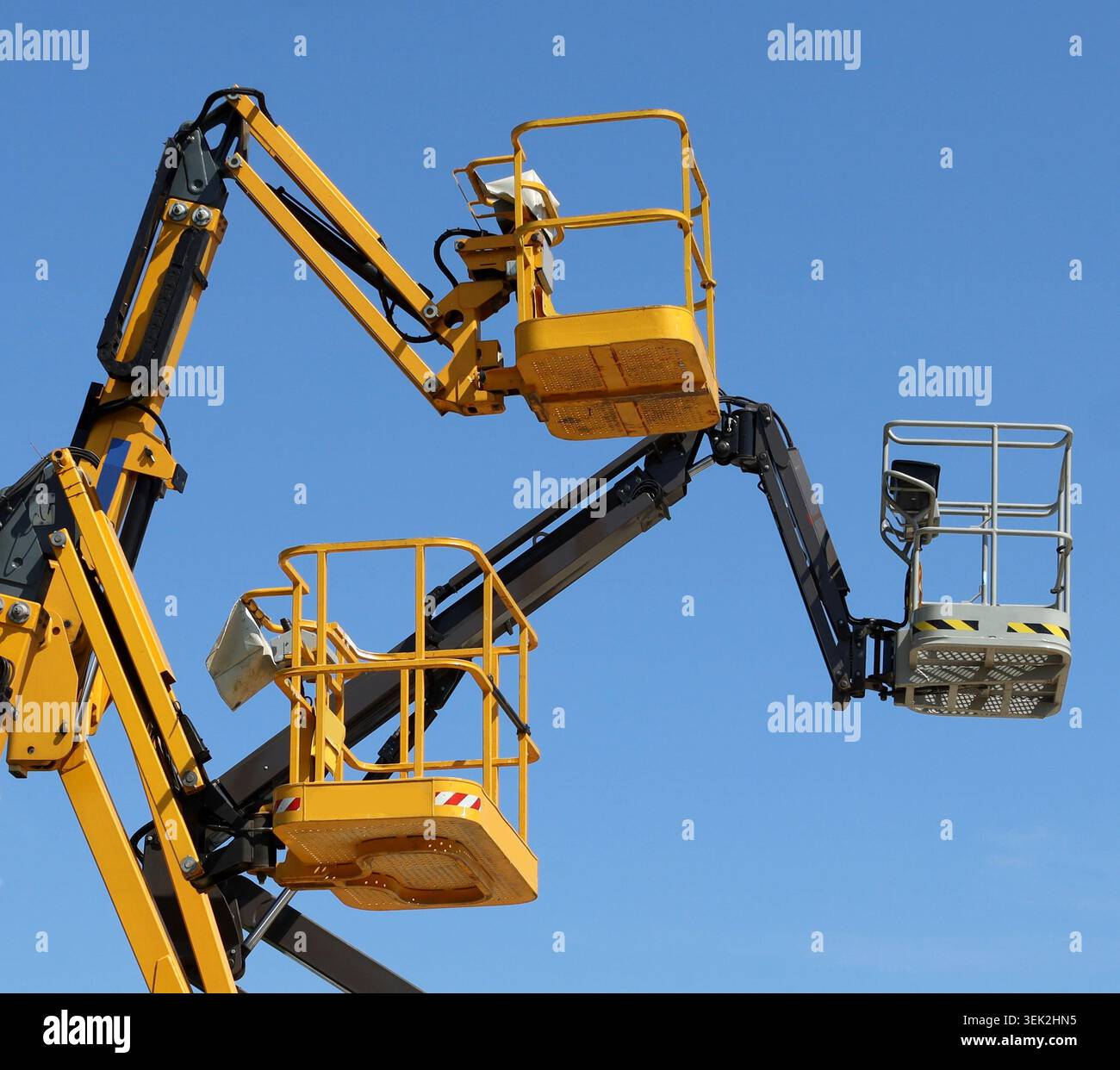 Drei Hubarbeitsbühnen mit Kirschpflücker, zwei gelbe und eine schwarze, vor blauem Himmel. Stockfoto