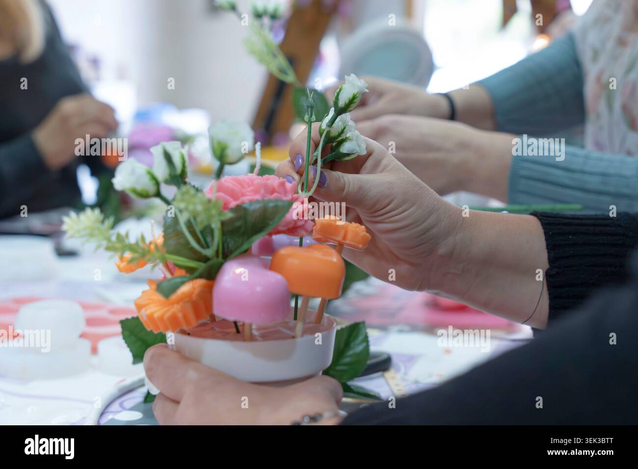 Die Menschen arrangieren mit Händen Wachsblumen und Herzen zu einem farbenfrohen, dekorativen Kerzenständer Stockfoto