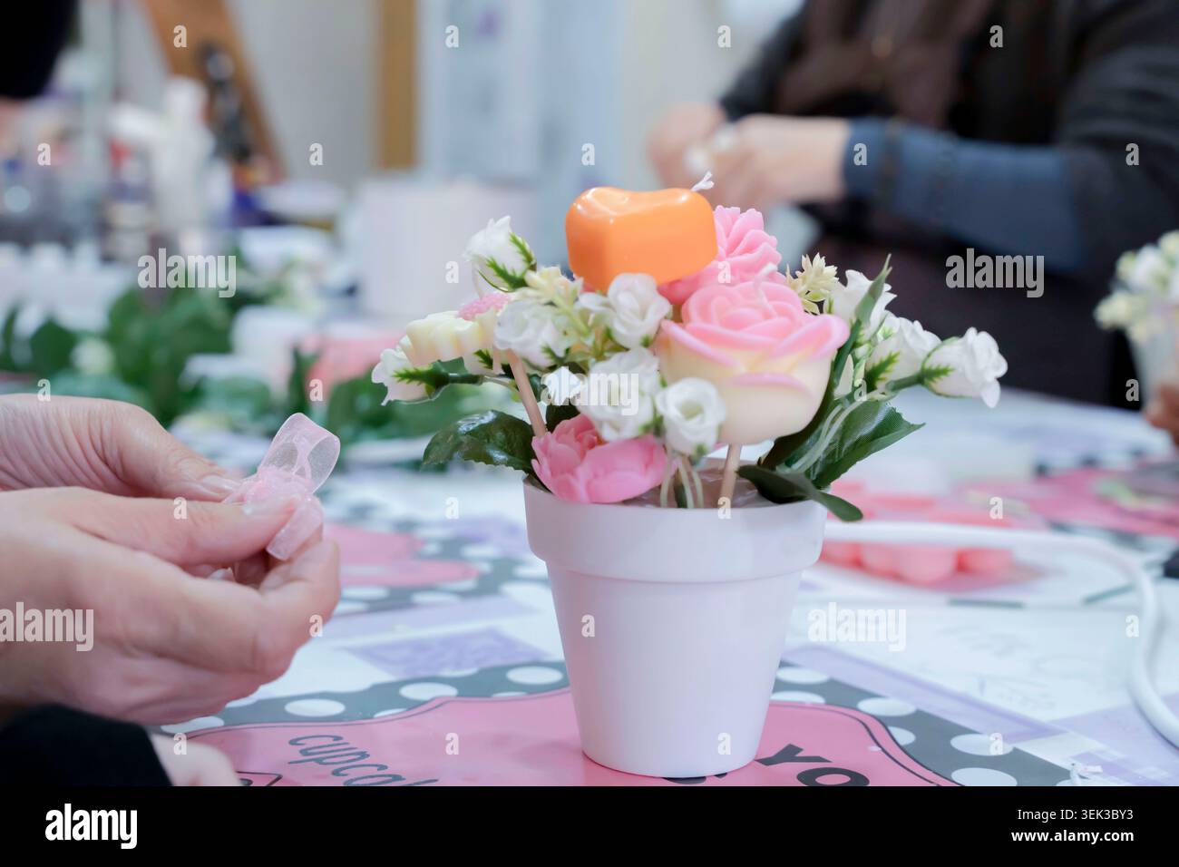 Hände kreieren ein wunderschönes Blumenarrangement mit dekorativen handgemachten Kerzen in einem Topf Stockfoto