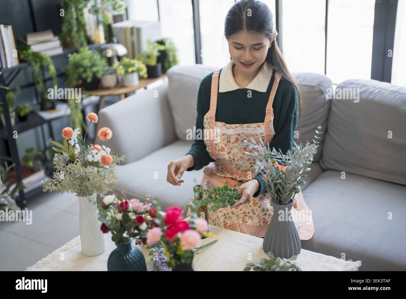 Glückliche asiatische Frau arrangiert Blumen und kümmert sich um das Grün zu Hause Stockfoto