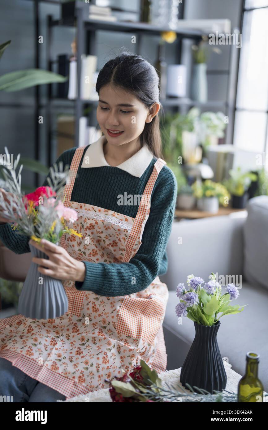 Glückliche asiatische Frau arrangiert Blumen und kümmert sich um das Grün zu Hause Stockfoto