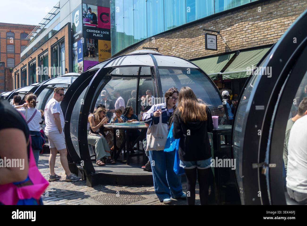 London, UK, 3. Mai 2026, zahlreiche futuristische, durchsichtige kuppelförmige Esskapseln aus Glas und schwarzen Metallrahmen sind auf einem Kopfsteinpflaster angeordnet Stockfoto