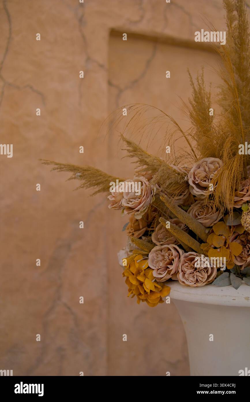 Blumenstrauß in Erdtönen gegen strukturierte Lehmwand mit stumpfem Rose und getrockneten Pampas Gras Blumenarrangement Stockfoto