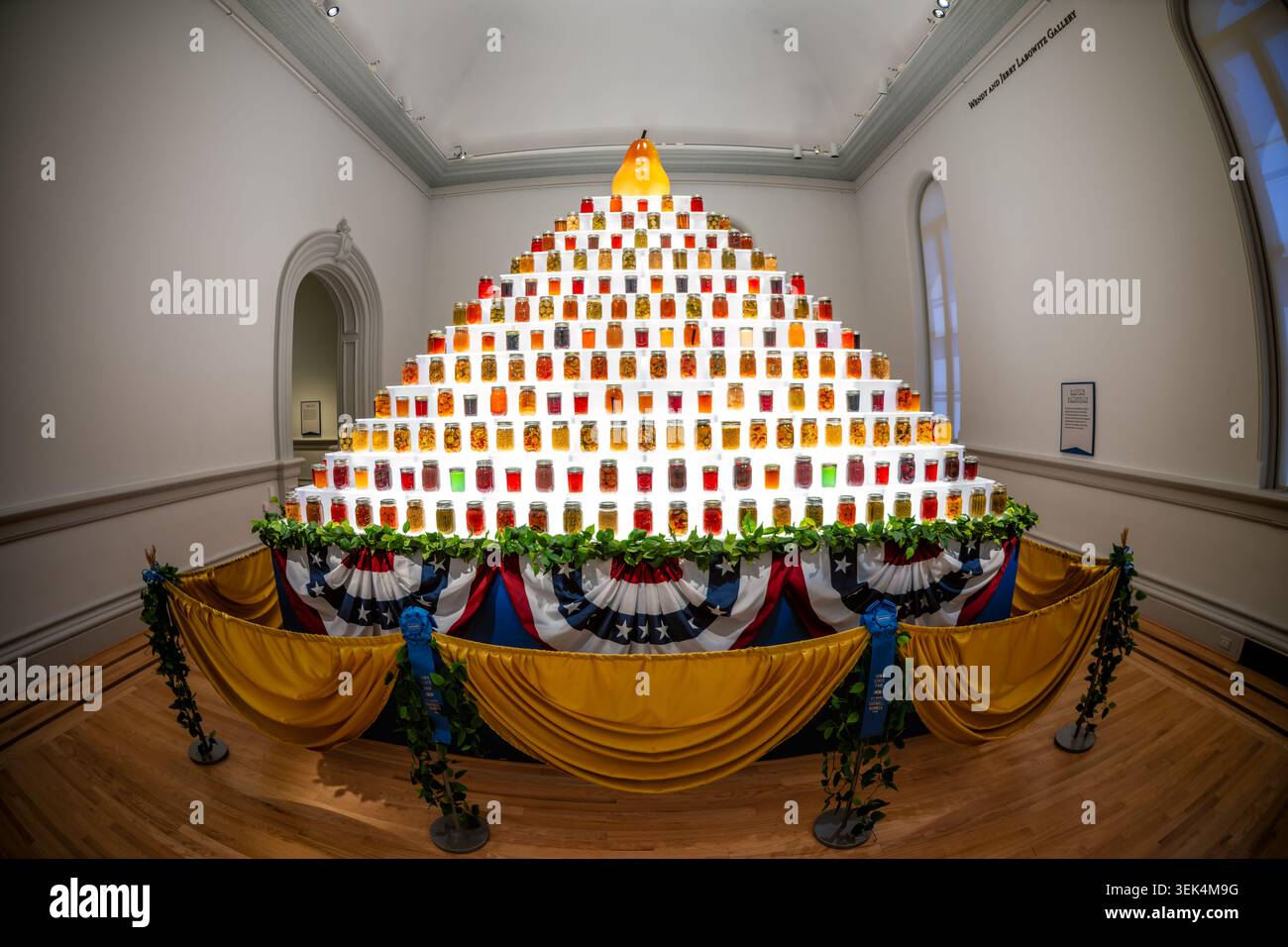 Home Canning Display Stufenpyramide Einmachgläser Glass Pear Washington DC Vereinigte Staaten | WASHINGTON D.C., Vereinigte Staaten — Eine Stufenpyramide aus mehr als 700 einmachgläsern, gekrönt von einer großen Glasbirne, bildet die Installation des Iowa State Fair Einmachungsmeisters Rod Zeitler in der Renwick Gallery. Die Glasbirne aus dem Jahr 1994 wurde von den Glaskünstlern Flora C. Mace und Joey Kirkpatrick aus Seattle gefertigt; die patriotischen Bündel und blauen Bänder der Ausstellung spiegeln die Preiskonservierungs- und Konservierungswettbewerbe des frühen 20. Jahrhunderts wider. Stockfoto