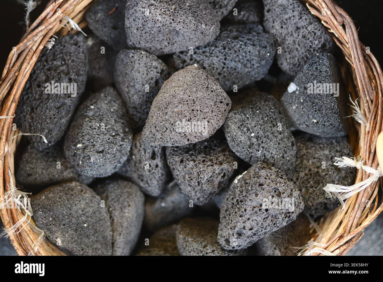 Sammlung von schwarzen Steinen in einem gewebten Korb Stockfoto