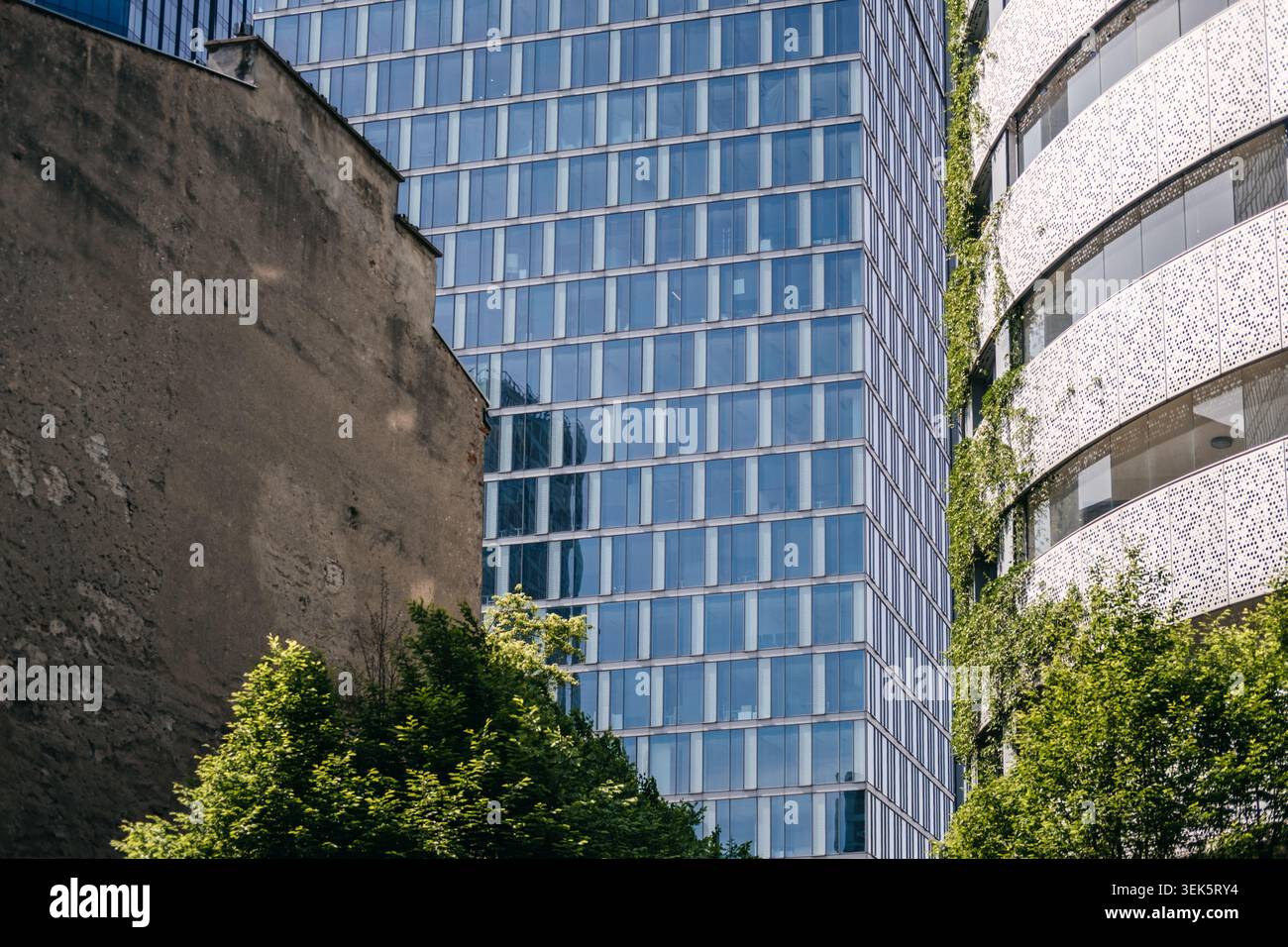 Alte Betonfassade steht im Kontrast zu modernen Glashochhäusern und grünen Wänden. Adaptive Reuse Construction Trend, historisch und Stockfoto
