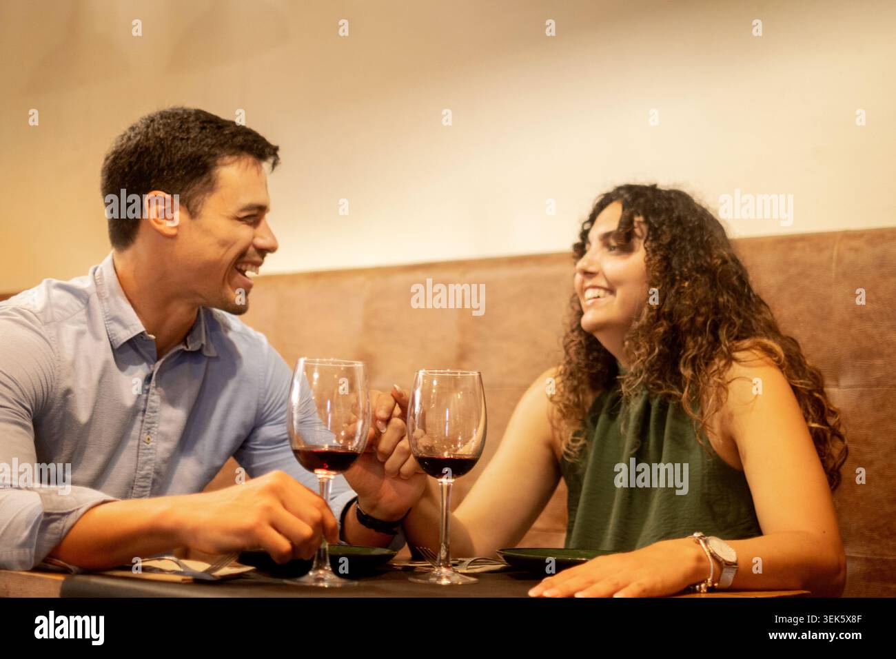 Junge Paare verbringen einen entspannten Moment zusammen, während sie Gläser Rotwein in einem gemütlichen Restaurant genießen. Romantisches kulinarisches Erlebnis, geselliges miteinander Stockfoto