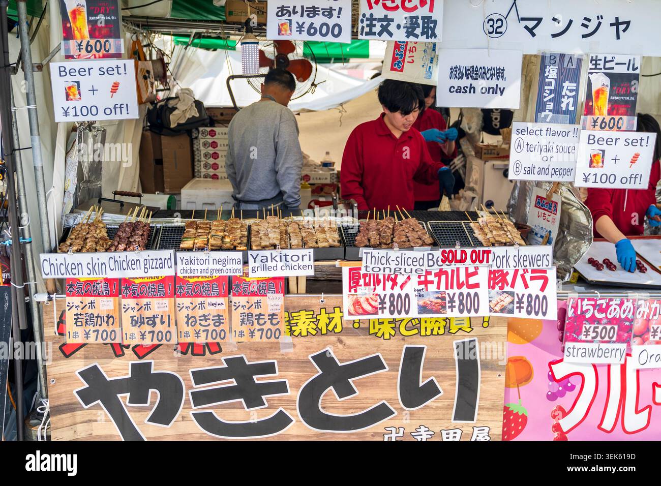 Theke eines Imbissstandes im Ueno Park, an dem verschiedene Snacks mit Hühnchen, Yakitori und Schweinefleisch angeboten werden. Etiketten in Japanisch und Englisch mit Preisen. Stockfoto