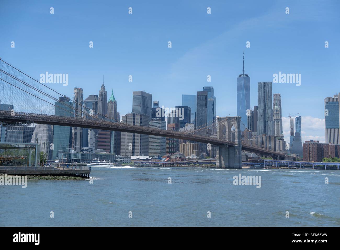 Die Brooklyn Bridge überspannt den Fluss mit der Skyline von manhattan unter einem klaren blauen Himmel. Stockfoto