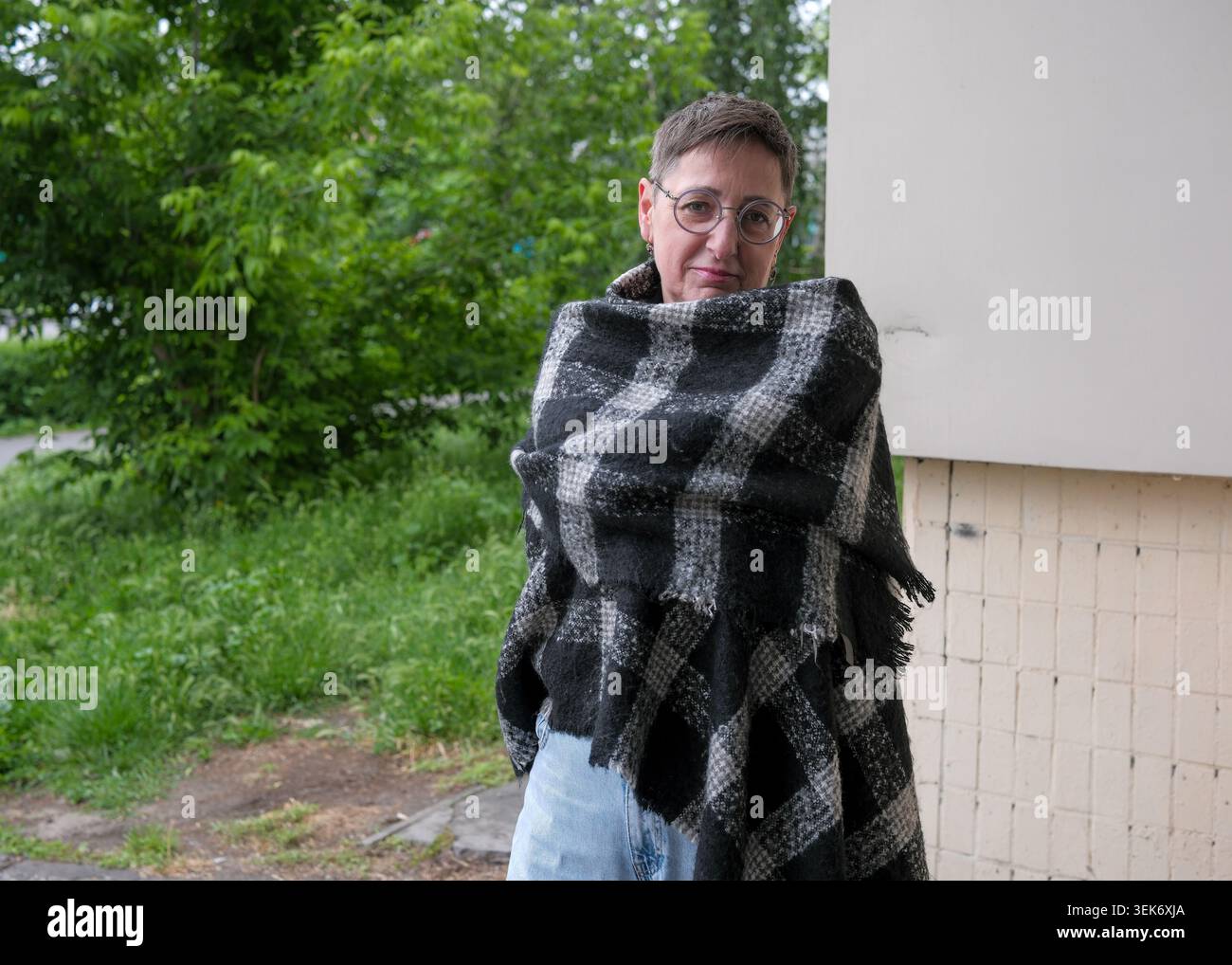 Eine Person steht ruhig, in eine gemütliche Decke gewickelt, umgeben von üppigem Grün. Stockfoto