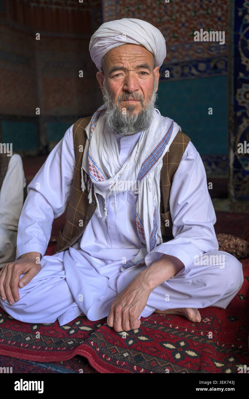 Mann in traditioneller Kleidung, der auf einem gemusterten Teppich in einer Moschee sitzt Stockfoto