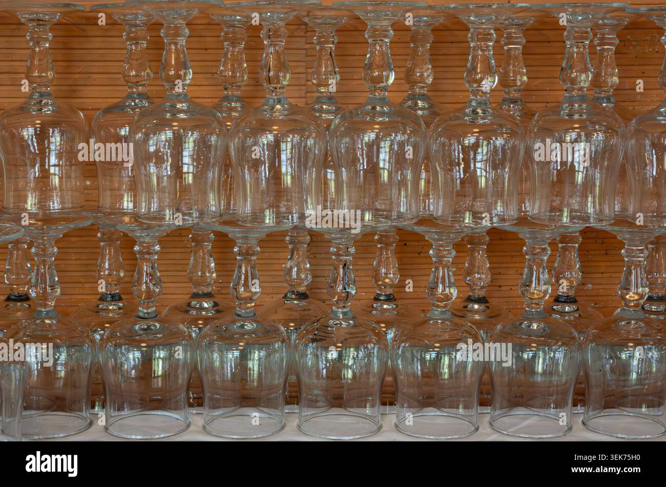 Ein Stapel klarer Gläser, die auf zwei symmetrischen Ebenen reflektiert werden, mit einer orangen Ziegelwand dahinter. Stockfoto