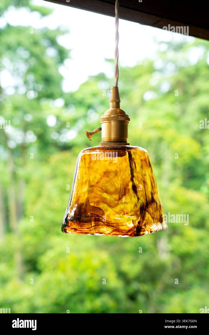 Eine rustikale, strukturierte Hängeleuchte aus braunem Glas mit einer Messingbuchse, die im Freien aufgehängt wird. Die warme Dekorationsleuchte hebt sich wieder schön hervor Stockfoto