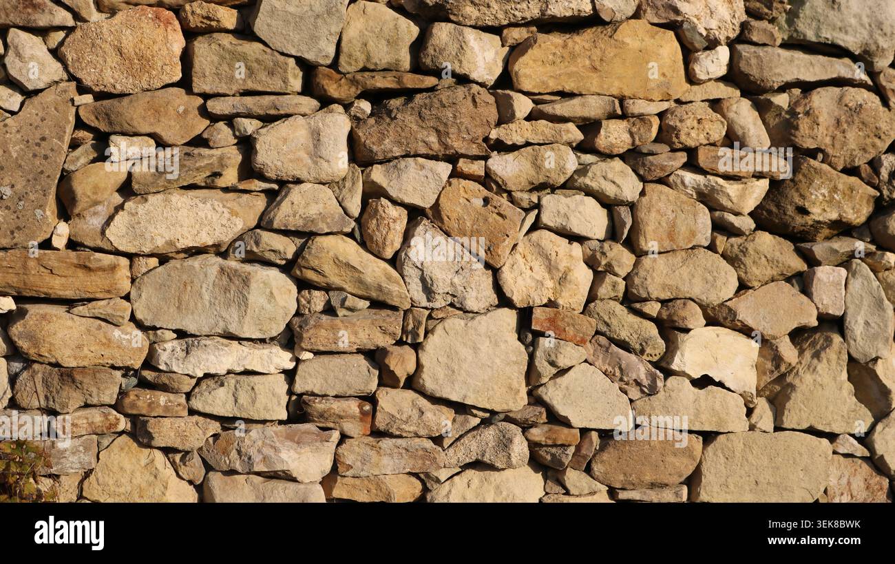 Eine Wand aus rauem Naturstein, die im Trockenverlegeverfahren verlegt wurde. Steine in verschiedenen Größen und Formen. Die Oberfläche der Steine ist rau, strukturiert Stockfoto