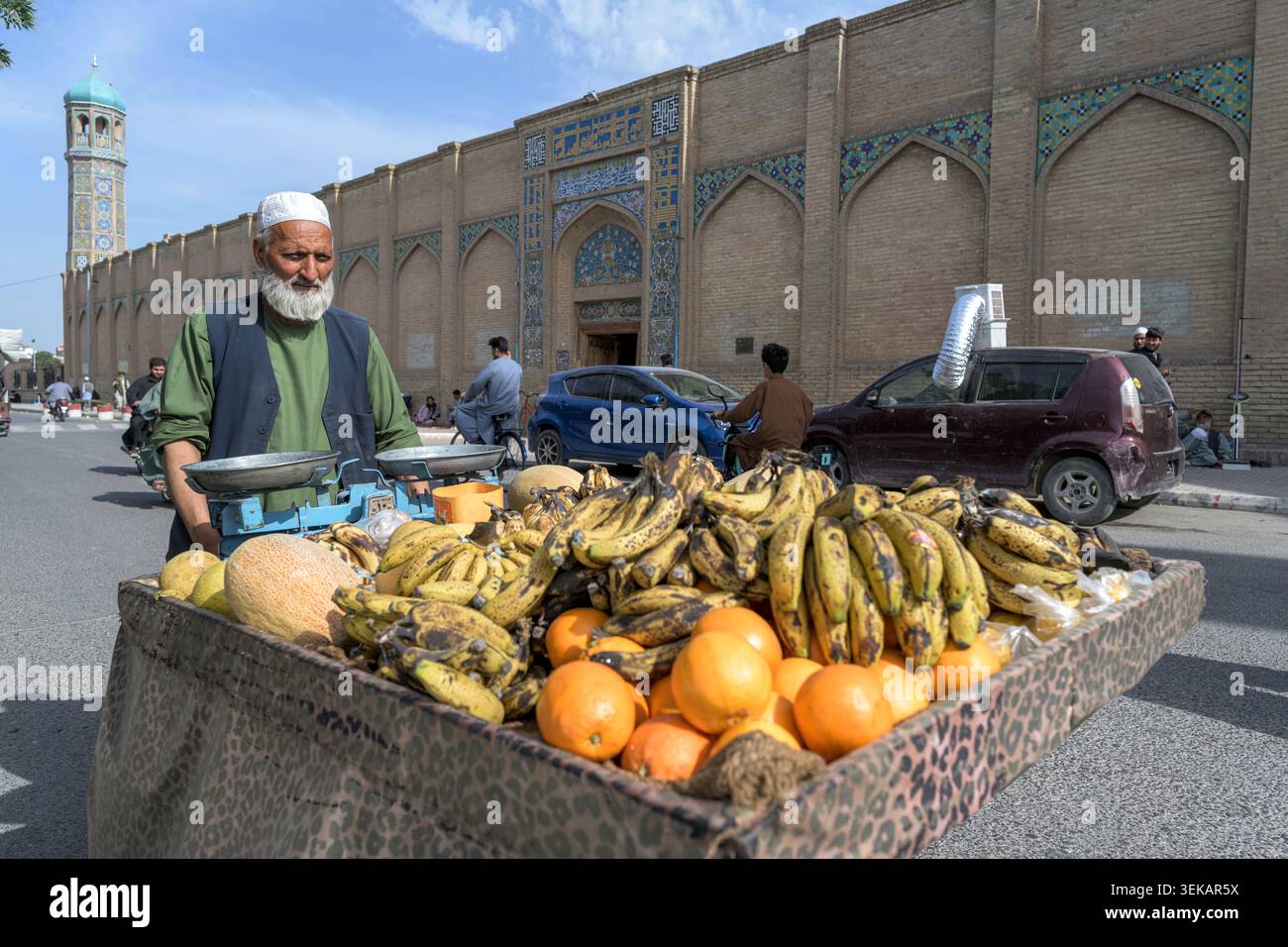 Straßenverkäufer, der mit einem Obstwagen mit Bananen, Orangen und Melonen vor der großen Moschee von Herat steht. Stockfoto