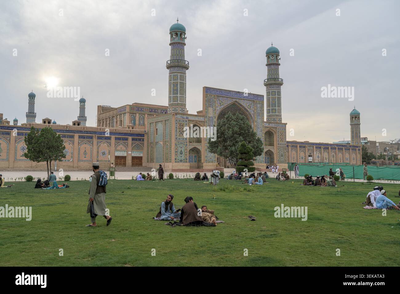 Menschen genießen einen offenen Grünraum vor der historischen freitagsmoschee, einem bedeutenden islamischen Architekturkomplex in afghanistan. Stockfoto