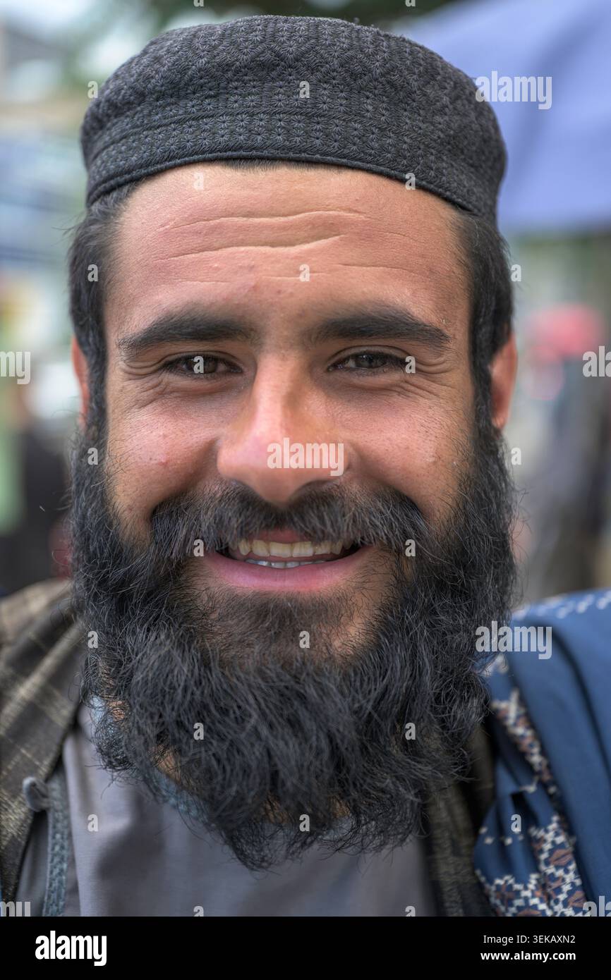 Afghane lächelt in die Kamera, trägt einen dunklen Bart und eine gemusterte Wollmütze, zeigt Glück. Stockfoto