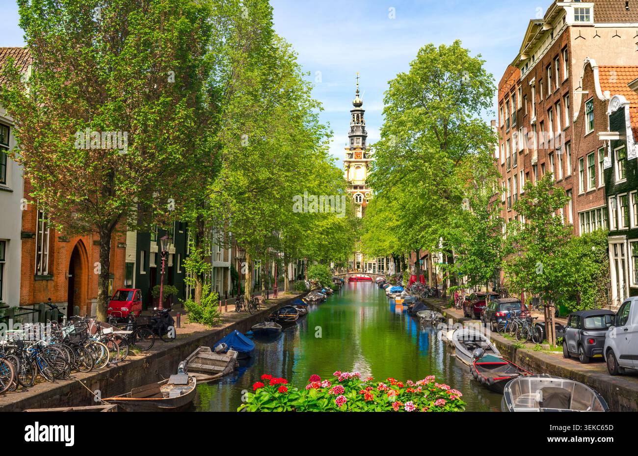 AMSTERDAM, NIEDERLANDE - 21. MAI 2026: Malerischer Blick auf den historischen Groenburgwal-Kanal, der von üppigen grünen Bäumen umgeben ist, mit angedockten Booten und den Ikonen Stockfoto
