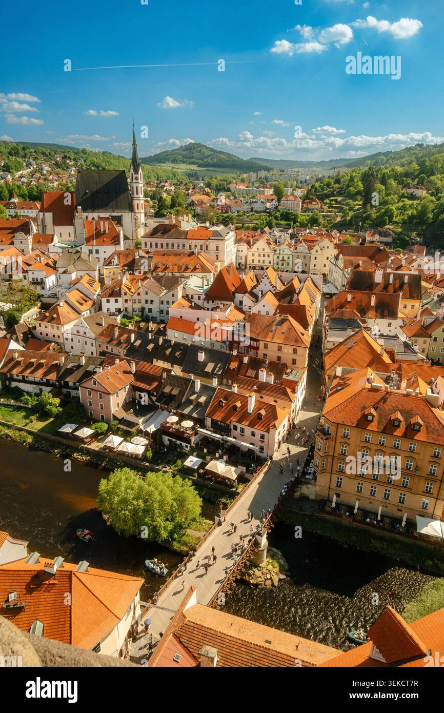 Aus der Vogelperspektive auf eine europäische Stadt am Fluss mit roten Dächern, Kirchturm und grünen Hügeln unter blauem Himmel Stockfoto