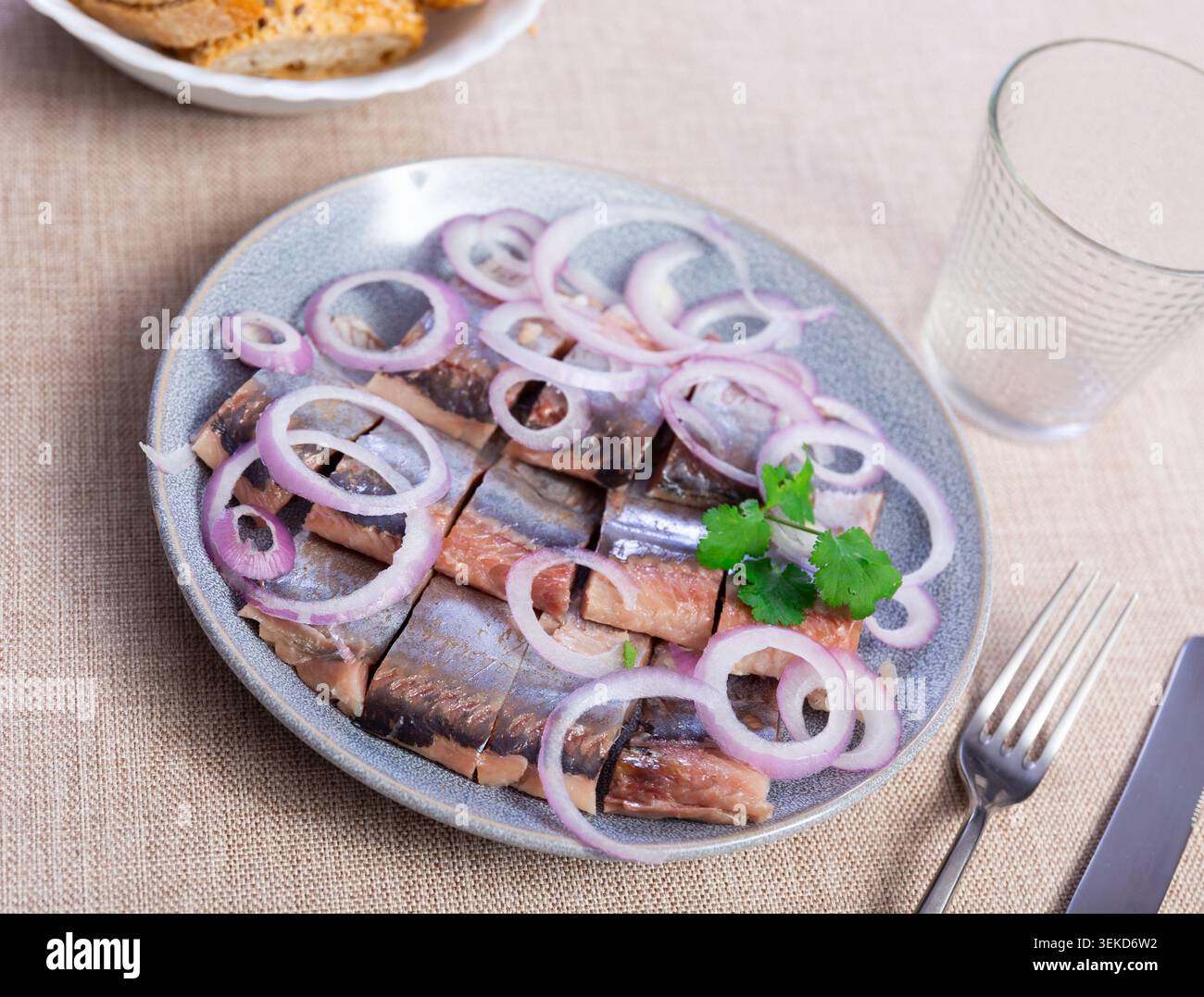 Auf hölzernen Tischständern Platte mit Stücken Heringsfilet, garniert mit Zwiebelringen und Petersilie Stockfoto