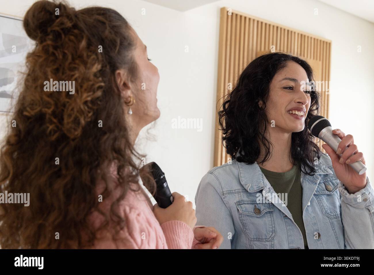 Zwei Freundinnen singen zusammen in einem kleinen Studio mit Mikrofonen in der Nähe von Akustiktafeln und gerahmter Kunst Stockfoto