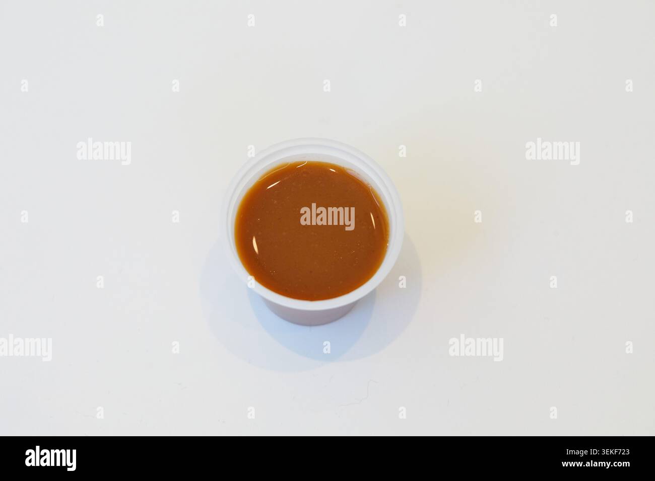 Braune herzhafte Soße in einem kleinen Plastiktopf auf weißem Hintergrund für Poke Schüsseln und asiatische Reisschalen. Stockfoto