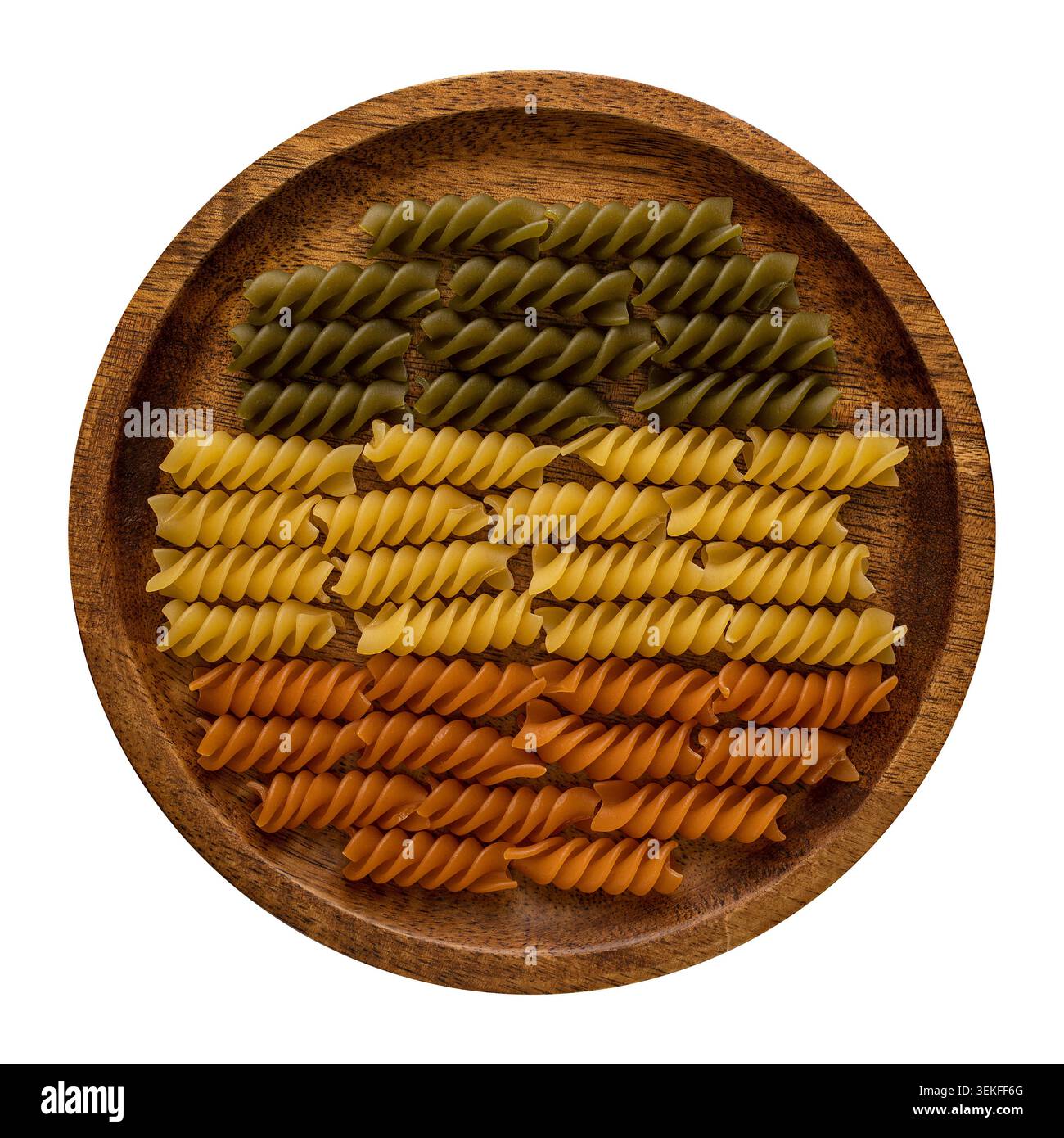 Dreifarbige Fusilli-Pasta in ordentlichen Reihen auf einem Holzteller von oben auf weißem Hintergrund. Stockfoto