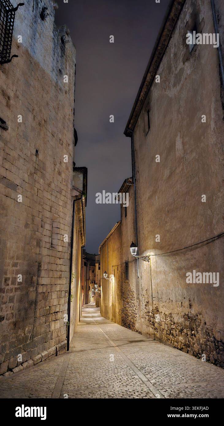 Enge mittelalterliche Kopfsteinpflasterallee, beleuchtet von Vintage Straßenlaternen bei Nacht zwischen alten Steinmauern in der historischen Altstadt von Girona, Spanien - Smartphone-aufgenommenes Stockfoto