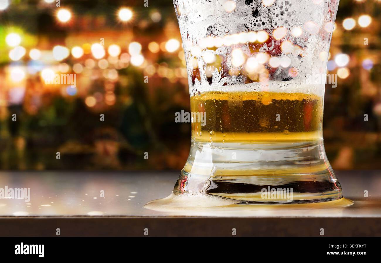 Nahaufnahme eines halb leeren Bierglases auf einem Tisch mit Schaum und Blasen, umgeben von warmen Bokeh-Lichtern in lebhafter Bar-Atmosphäre. Stockfoto