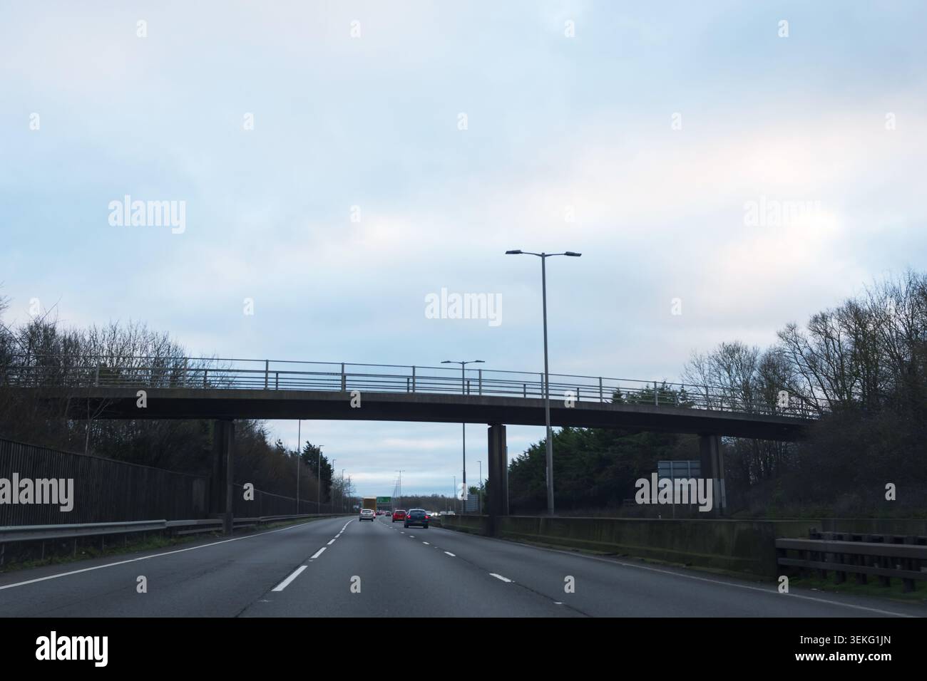 Der Verkehr fließt an einem bewölkten Tag entlang einer mehrspurigen Autobahn unter einer Betonüberführung, wobei Autos und LKWs in Richtung Horizont fahren und m fördern Stockfoto