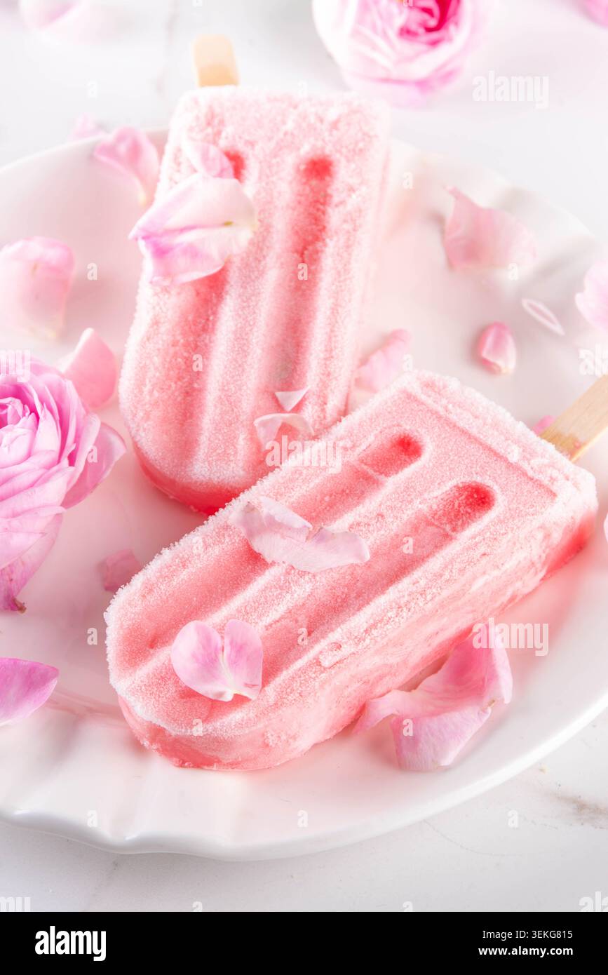 Süße Kräuterrose Eis Lollies in Sticks, leckerer cremiger Tee Rose Blumen gefrorenes Dessert mit Rosenknospen auf weißem Marmor Tisch Backgr Stockfoto