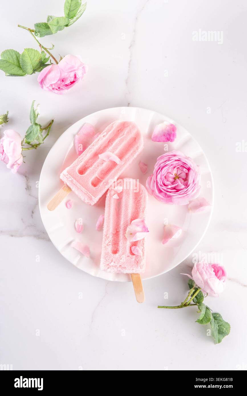 Süße Kräuterrose Eis Lollies in Sticks, leckerer cremiger Tee Rose Blumen gefrorenes Dessert mit Rosenknospen auf weißem Marmor Tisch Backgr Stockfoto