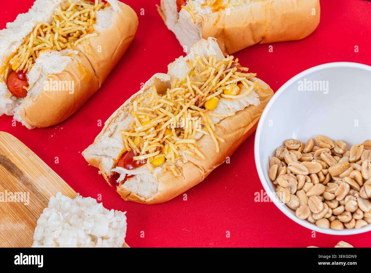 Overhead Shot zeigt lebendige brasilianische Hot Dogs auf roter Oberfläche. Konzentrieren Sie sich auf die Texturen von Kartoffelstäbchen und weichen Brötchen. Kommerzielles Image für Fast-Food-Concept Stockfoto