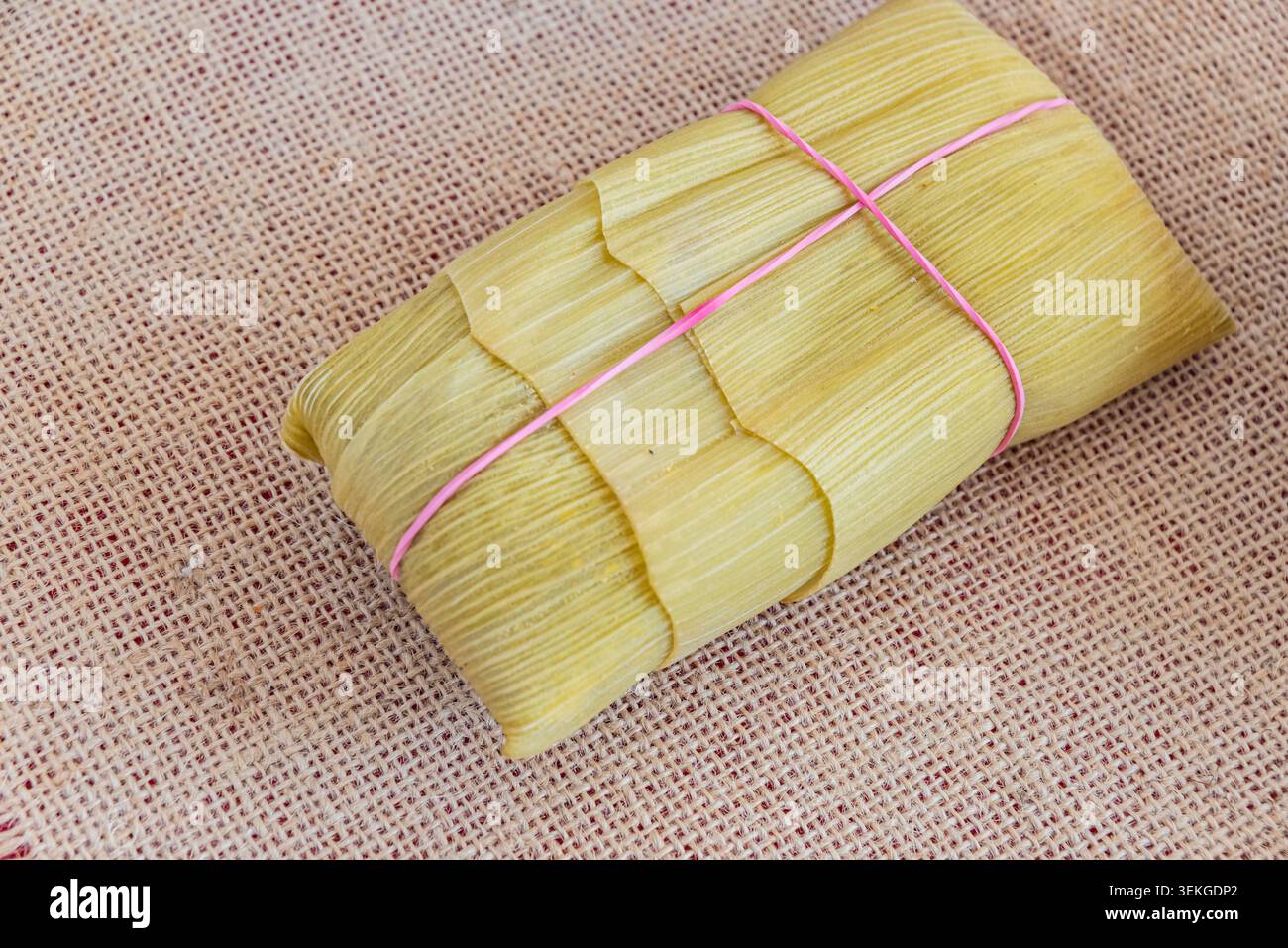 Pamonha auf Sackleinen, traditionelle brasilianische Küche. Zubereitet mit frischem Mais, gebunden mit rosa Schnur. Studio-Aufnahme zeigt Texturen und neutrales Licht, ich Stockfoto