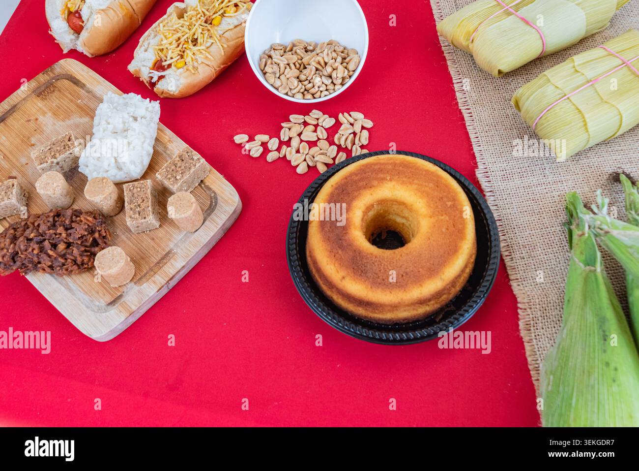 Ein Kopfschuss mit einem Ringkuchen, Erdnüssen, Maisschalen, Hot Dogs und Süßigkeiten auf einem roten Tisch. Weiches natürliches Licht sorgt für lebendige Farben, geeignet Stockfoto