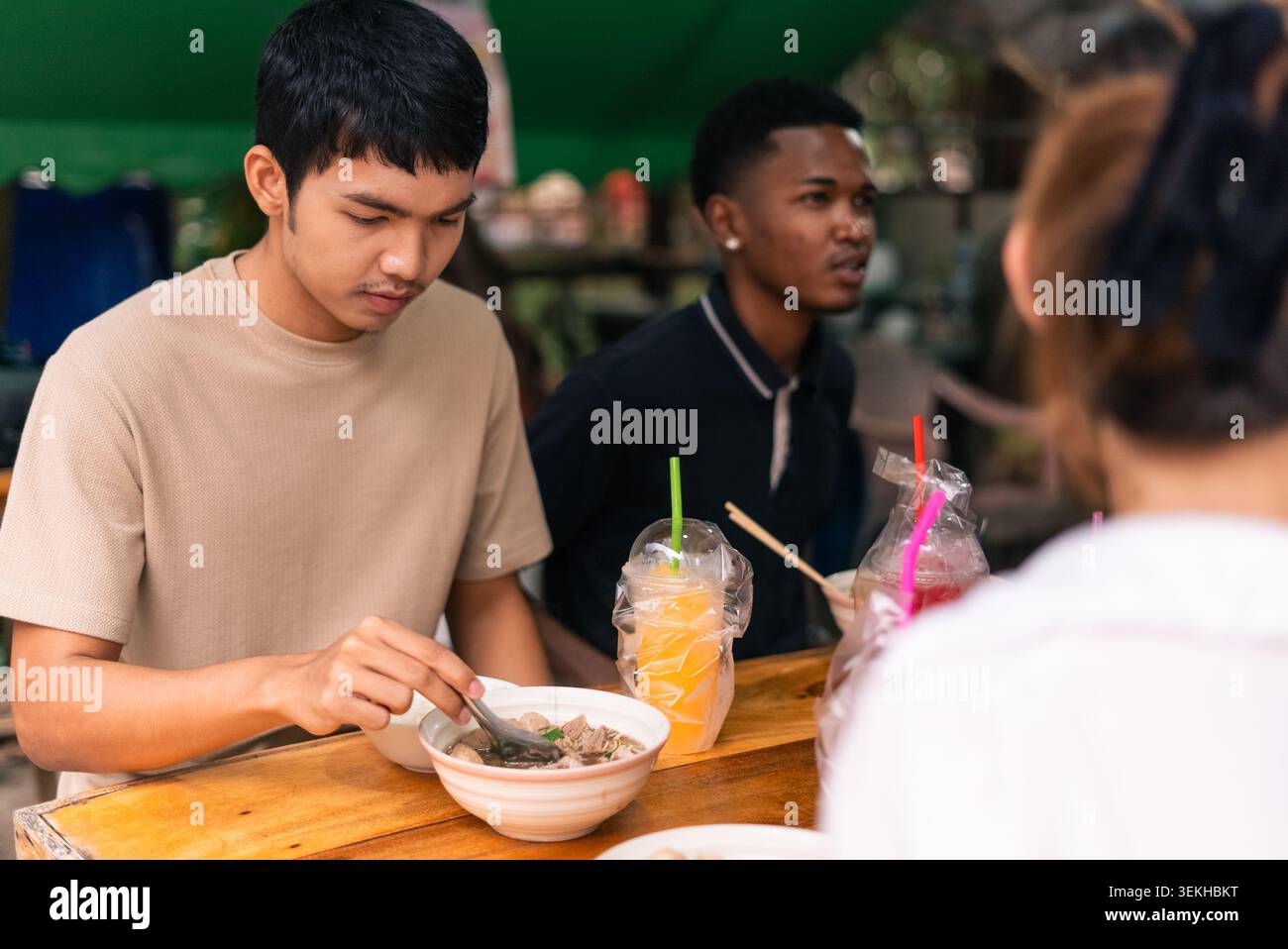 Junge Menschen genießen Streetfood und Getränke an einem Marktstand im Freien Stockfoto