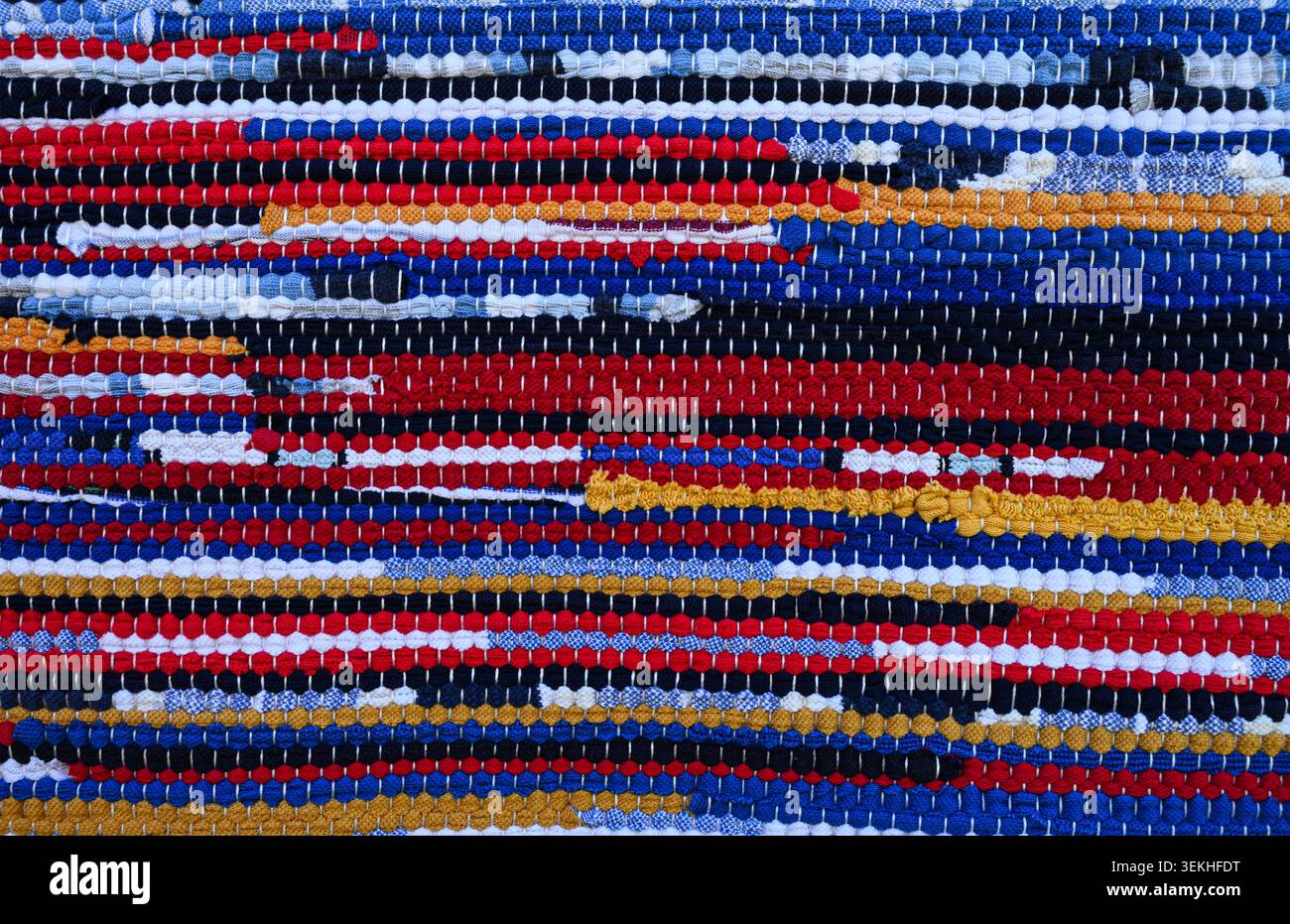 Farbenfrohe gewebte Teppichstruktur mit hellen Streifen und handgefertigten Textil-Details. Rustikaler Stoffhintergrund für Boho-Innenräume. Stockfoto