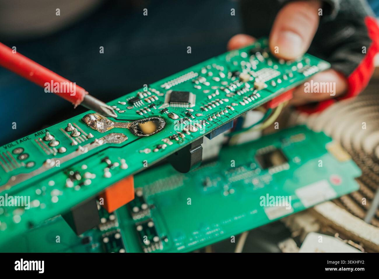 Nahaufnahme eines Technikers, der einen Lötkolben verwendet, um eine verbrannte und beschädigte elektronische Leiterplatte zu reparieren, und zeigt die komplizierten Komponenten und die Präzision, die bei der Reparatur der Elektronik erforderlich ist Stockfoto