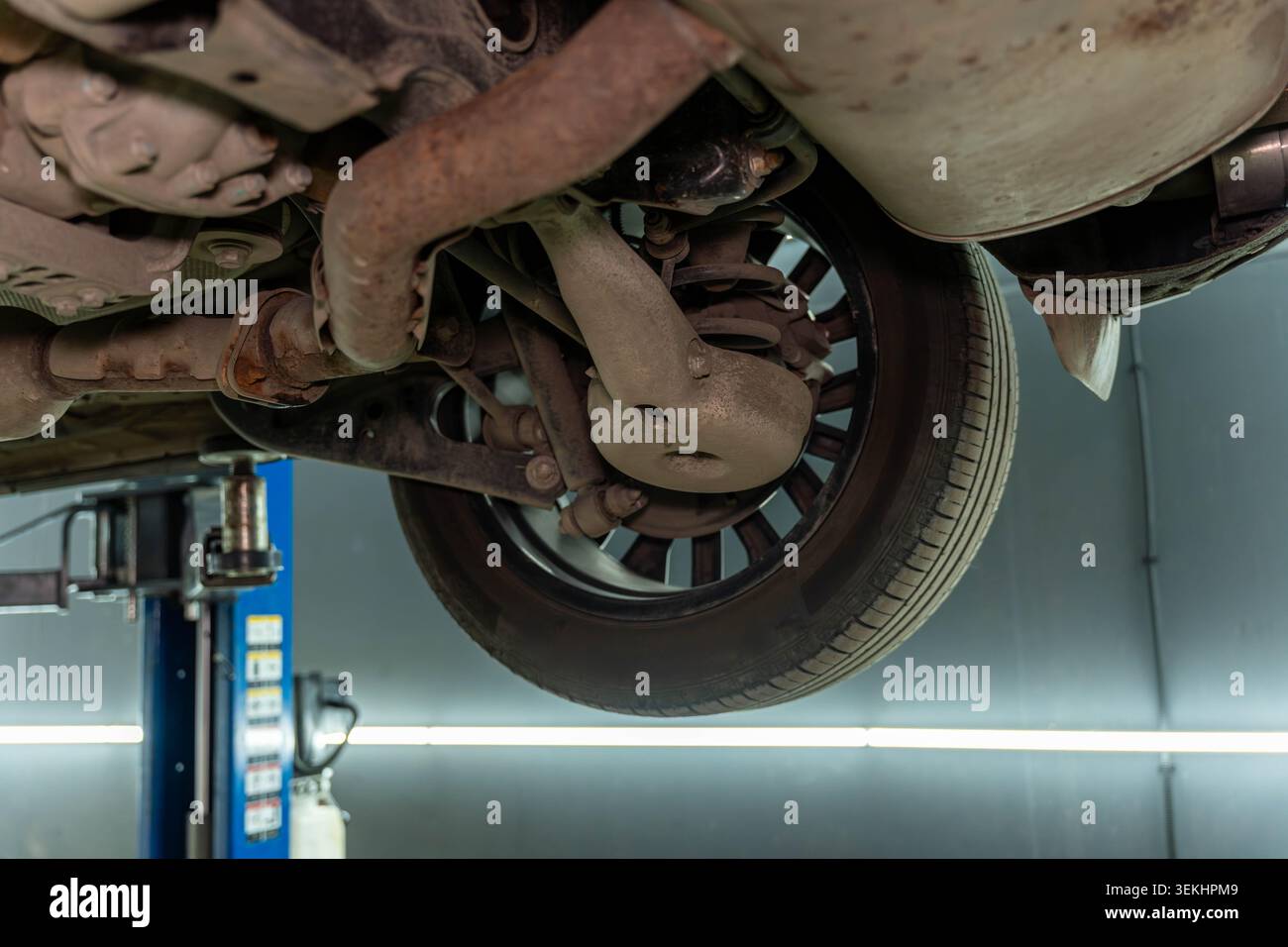 Niedrige Winkelansicht eines Fahrzeugs, das auf einer Servicehube angehoben wird, mit Unterwagen, Rad, Aufhängeteilen, rostfreien Metalloberflächen, und Industriewerkstatt Stockfoto