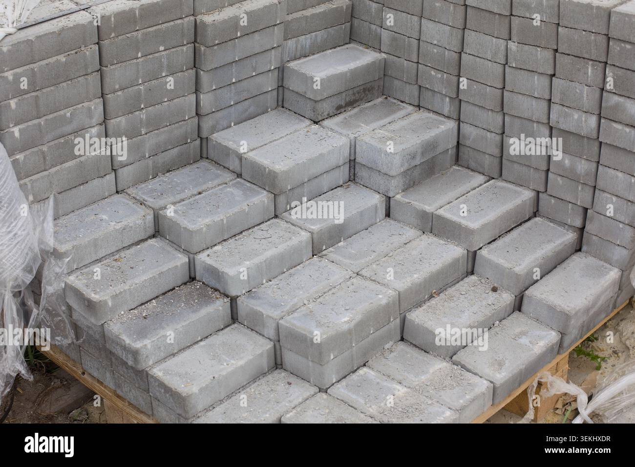 Ein ordentlich gestapelter Haufen grauer Betonpflastersteine auf einer Holzpalette, die für Bauarbeiten vorbereitet ist. Stockfoto