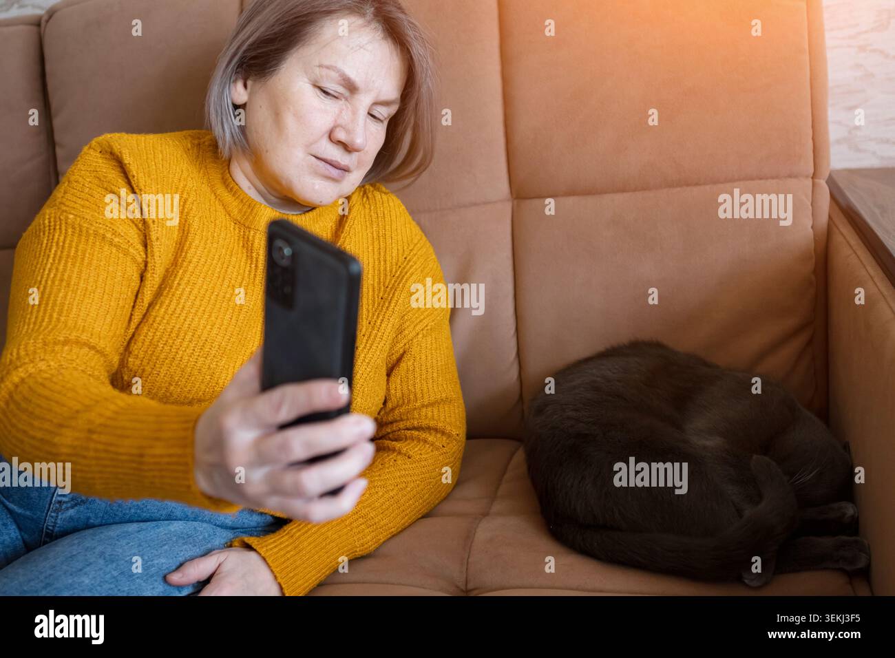 Frau, die sich auf dem Sofa mit Smartphone neben dem schlafenden Haustier entspannt Stockfoto