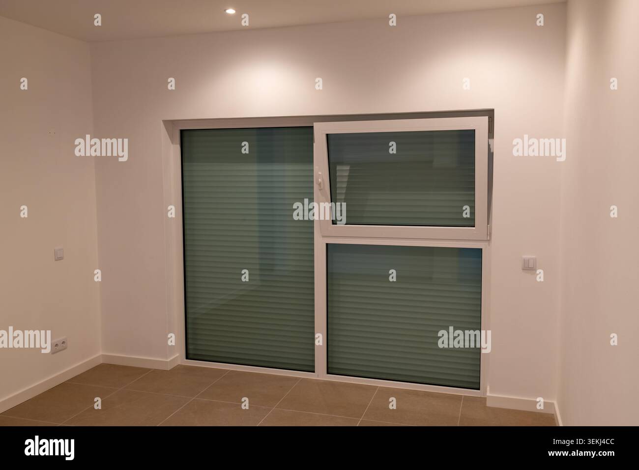 Das moderne Zimmer verfügt über weitläufige Glasschiebetüren mit integrierten horizontalen Jalousien, die eine elegante und minimalistische Ästhetik für Wohnsitze bieten Stockfoto